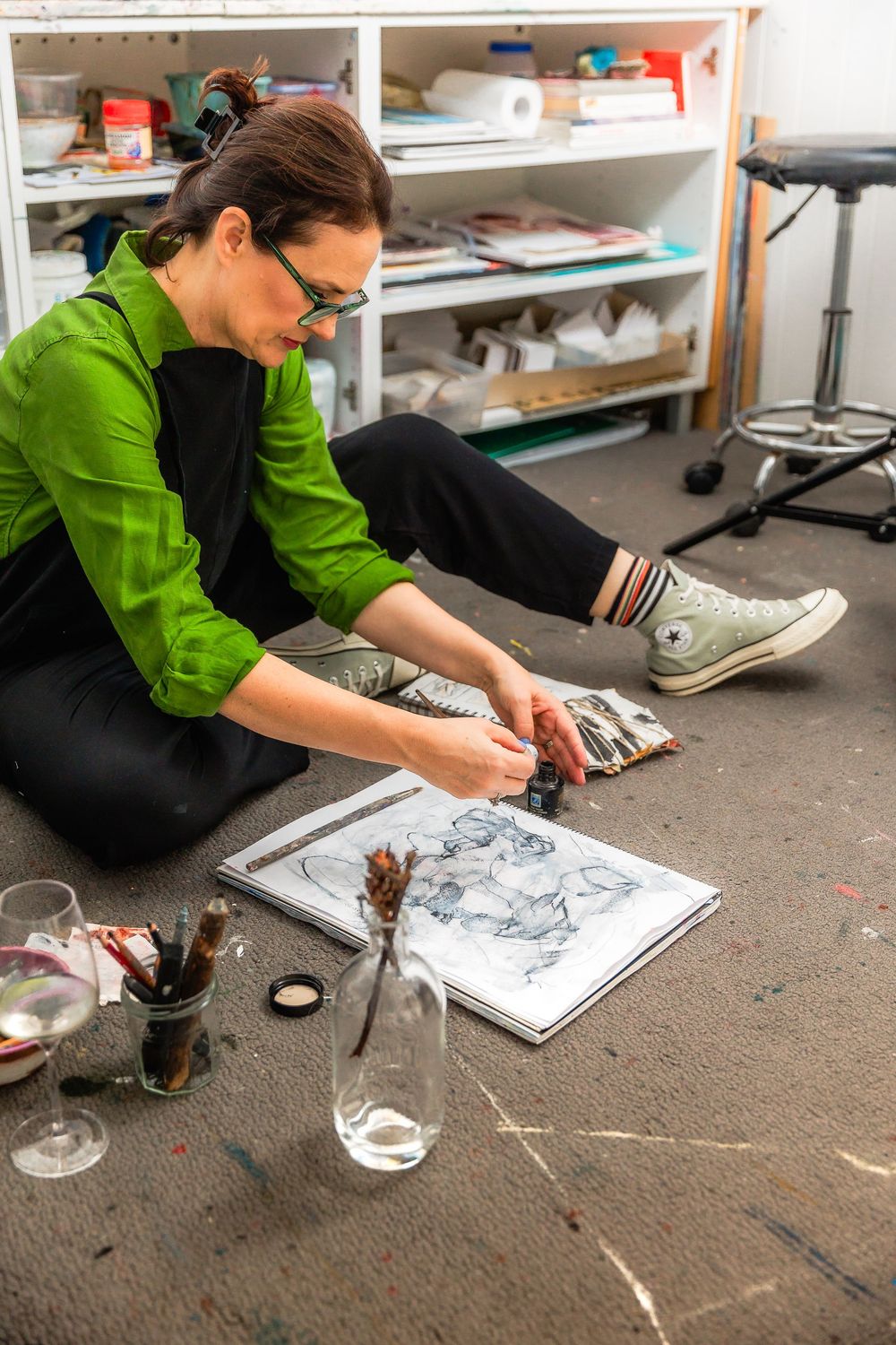 Artist sketching on floor while sitting among art supplies.