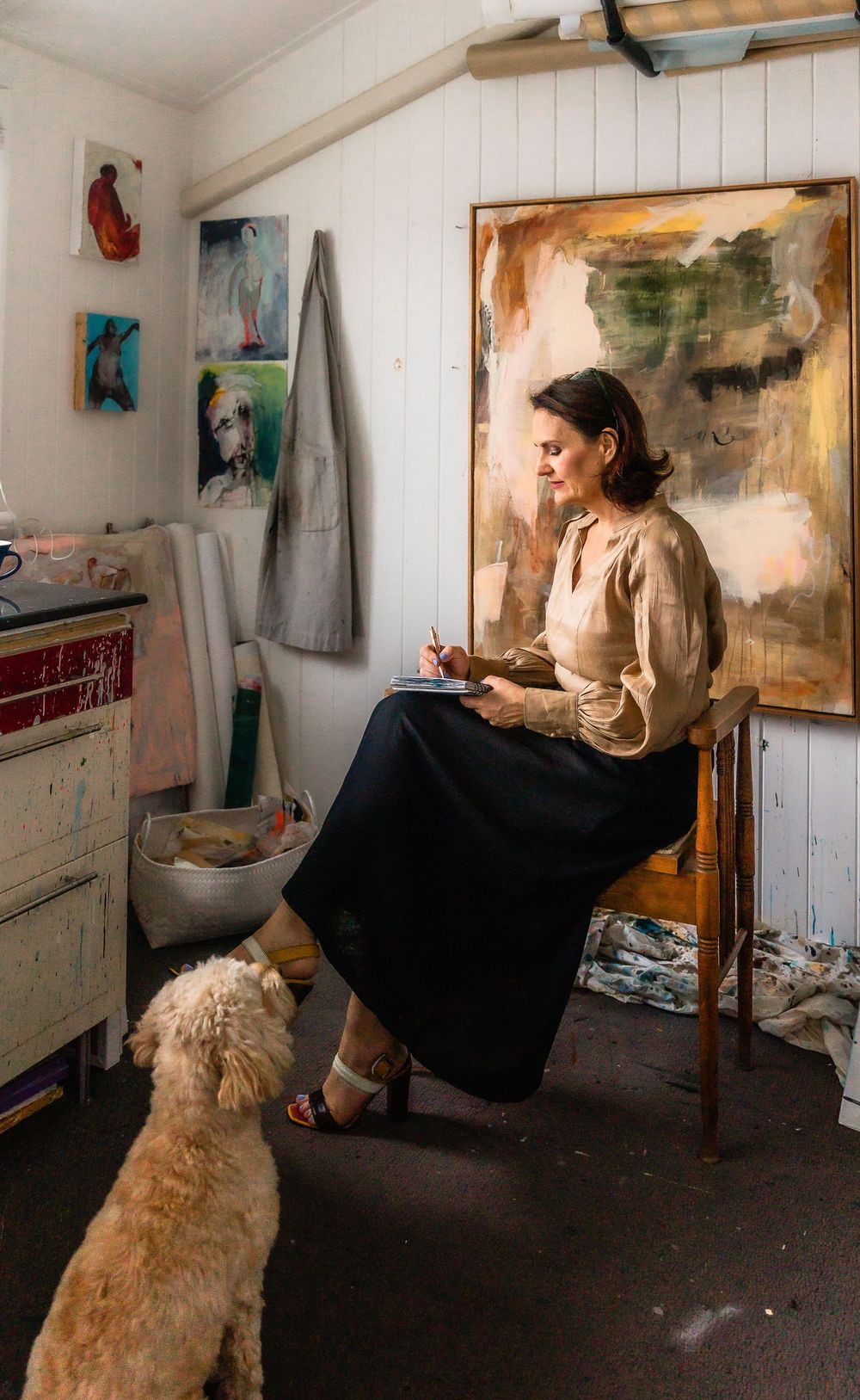 A series of photos showing an artist working in a studio with a large abstract painting and a golden retriever nearby.