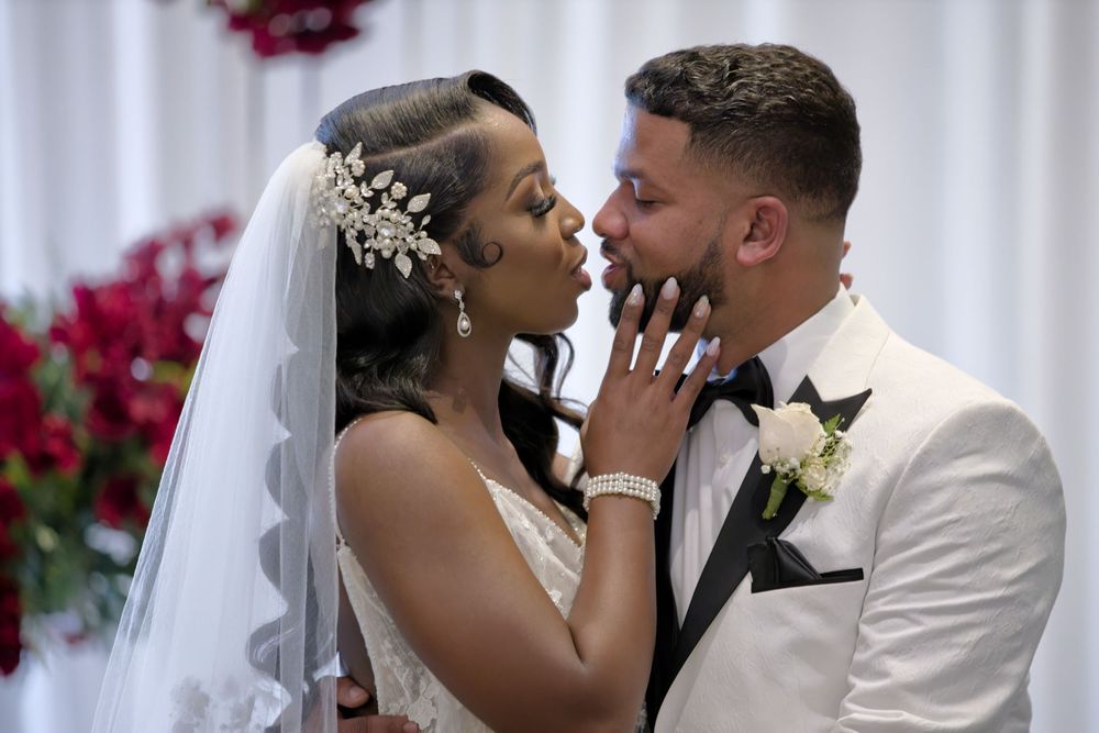 A bride and groom share an intimate moment during their wedding ceremony with red floral decor.