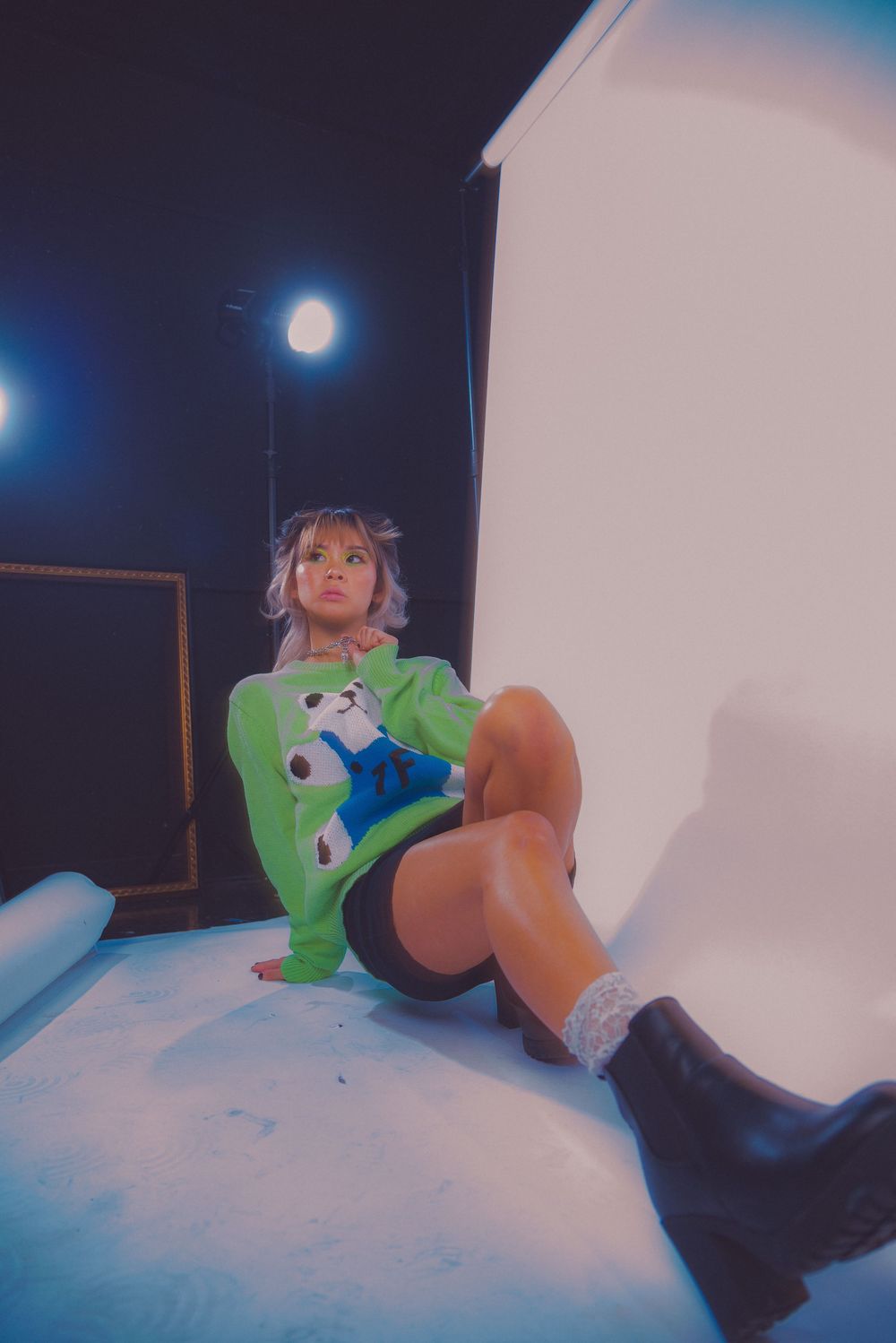 Artistic photoshoot on white backdrop featuring green sweater and black boots.