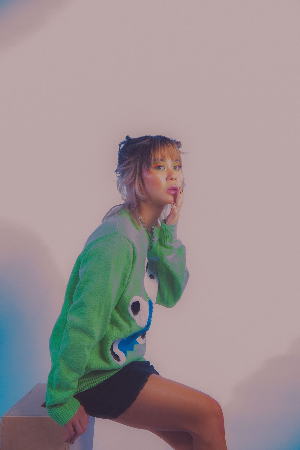 Stylish pose in neon green sweater and black shorts against light background.
