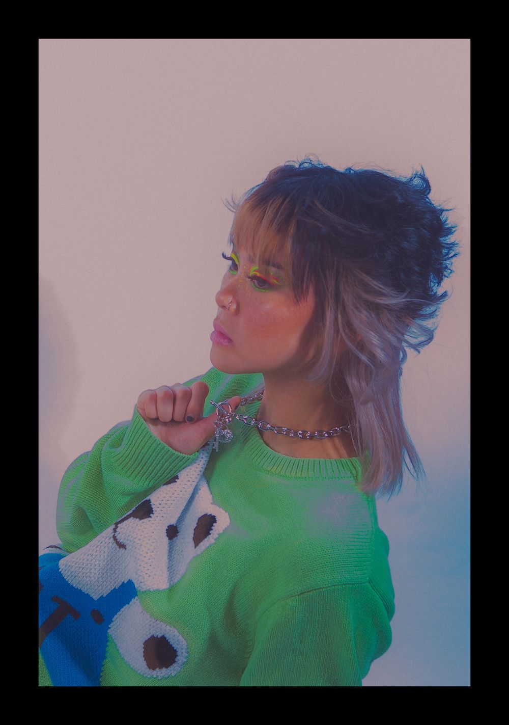 Side profile pose in vibrant green sweater with silver chain accessories.