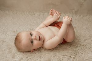 A baby lies on a soft cream-colored carpet while playing with their toes in a series of connected photos.