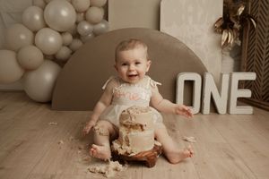 A first birthday celebration setup with neutral balloons, a cake smash session, and a 'ONE' sign in a beige room.