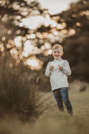A young child stands in a field at golden hour with bokeh lights in the background.