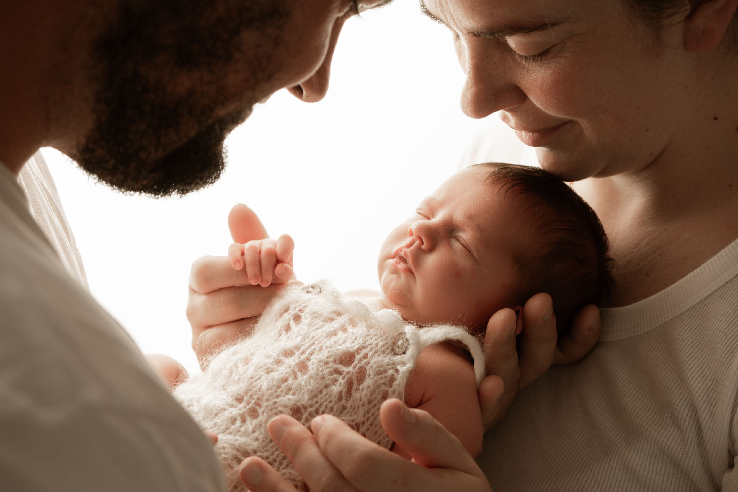 A tender moment between parent and newborn baby in soft natural lighting against a white background.