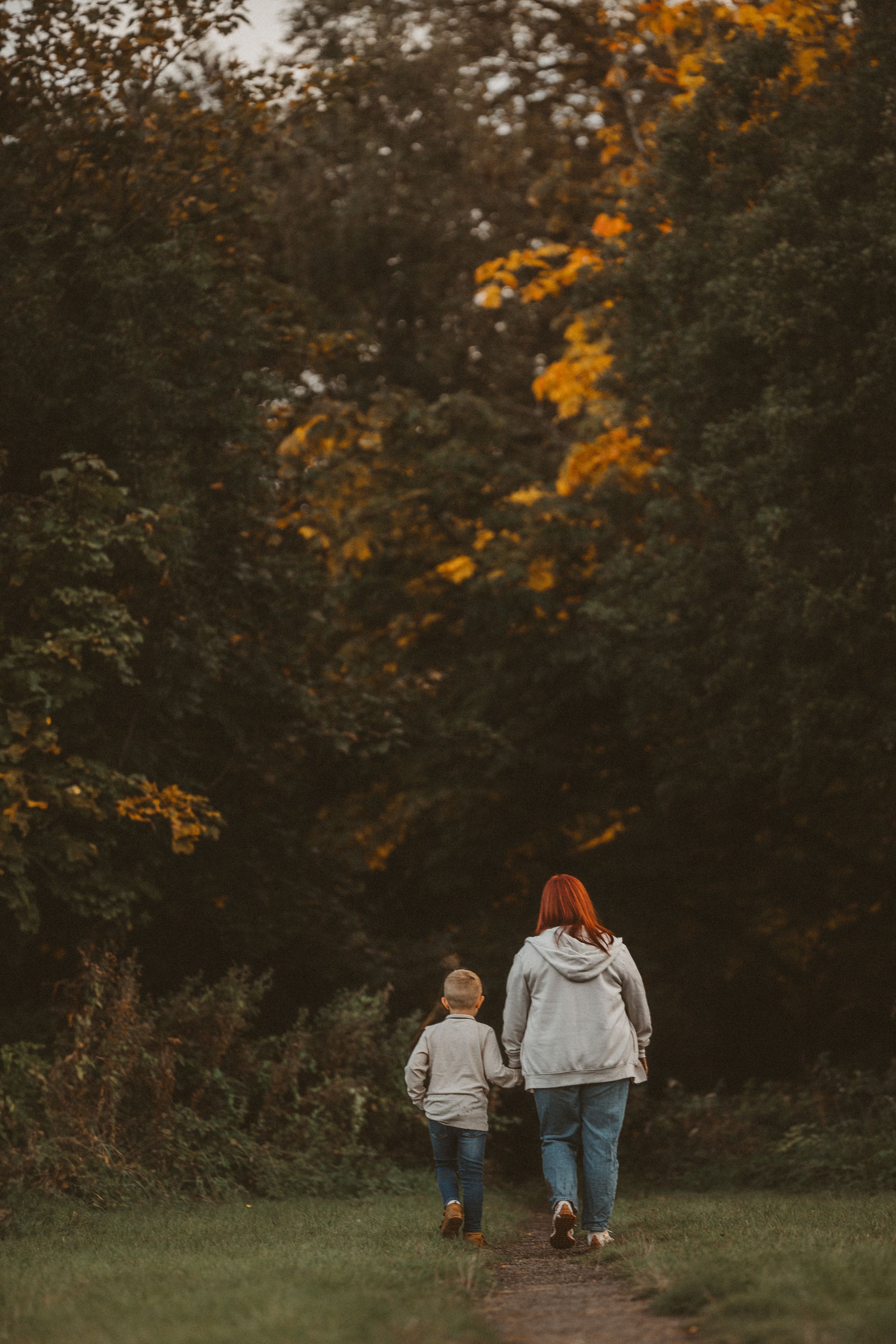Family taking an autumn walk together on a wooded path with golden fall foliage visible in the trees above.