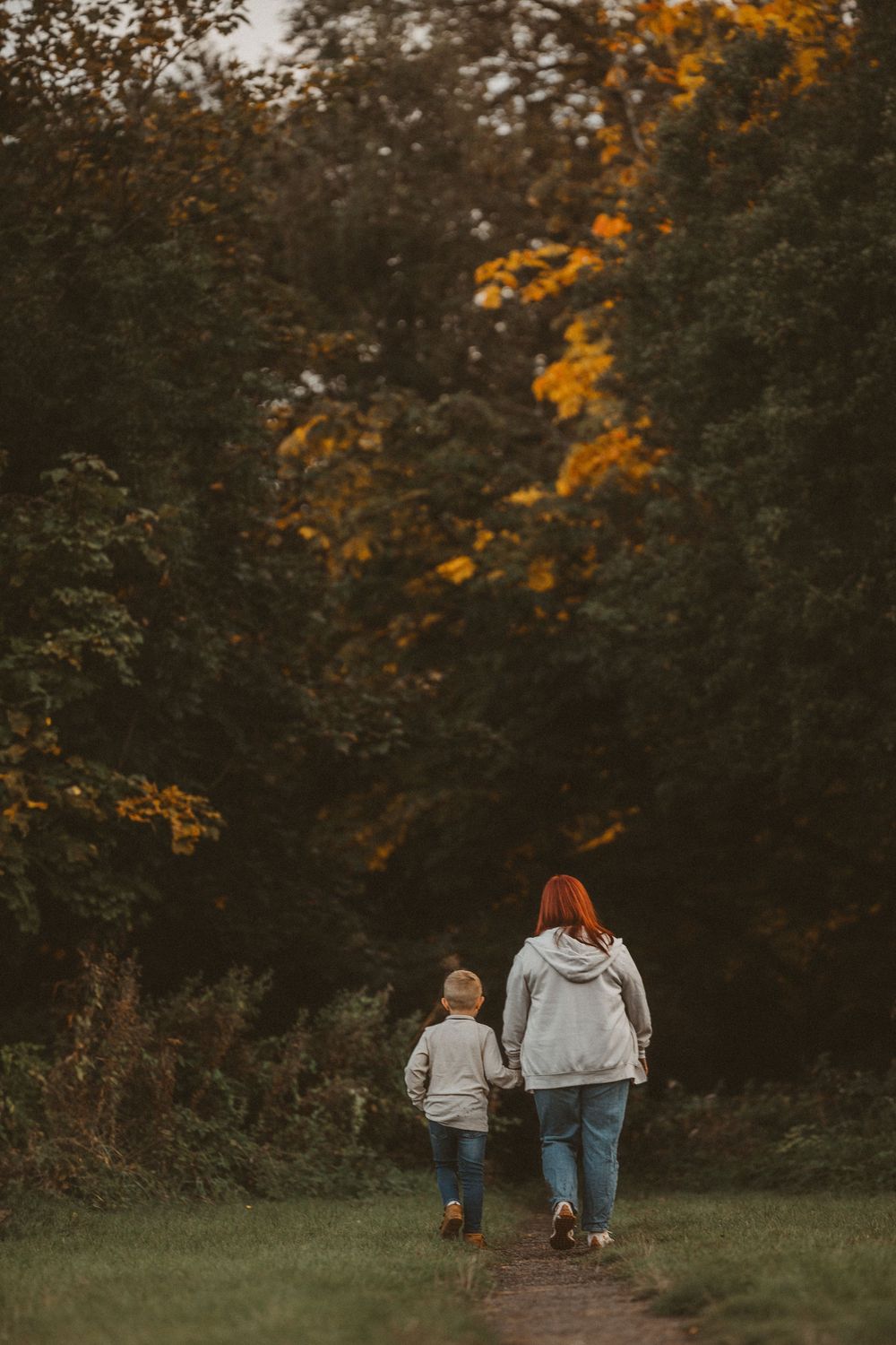 Family taking an autumn walk together on a wooded path with golden fall foliage visible in the trees above.