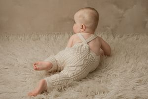 A baby wearing a white knit sweater crawls on a textured cream-colored carpet.