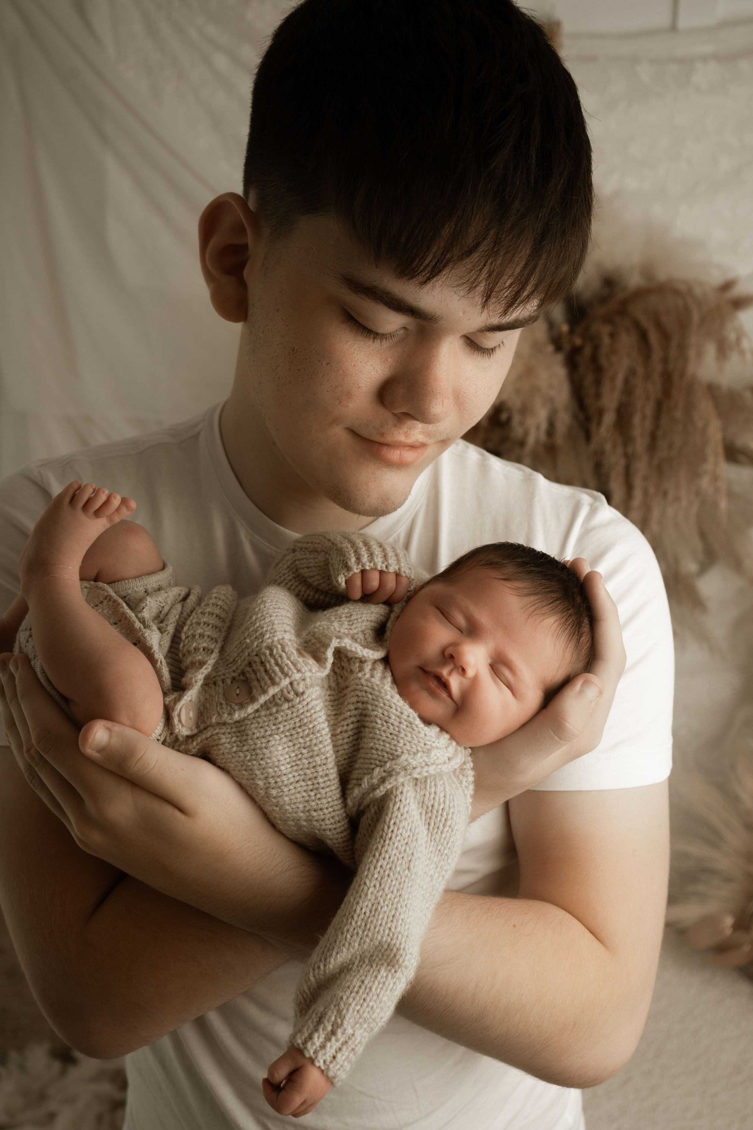 A tender newborn photography session showing a baby wrapped in a soft knit blanket being held against white fabric.