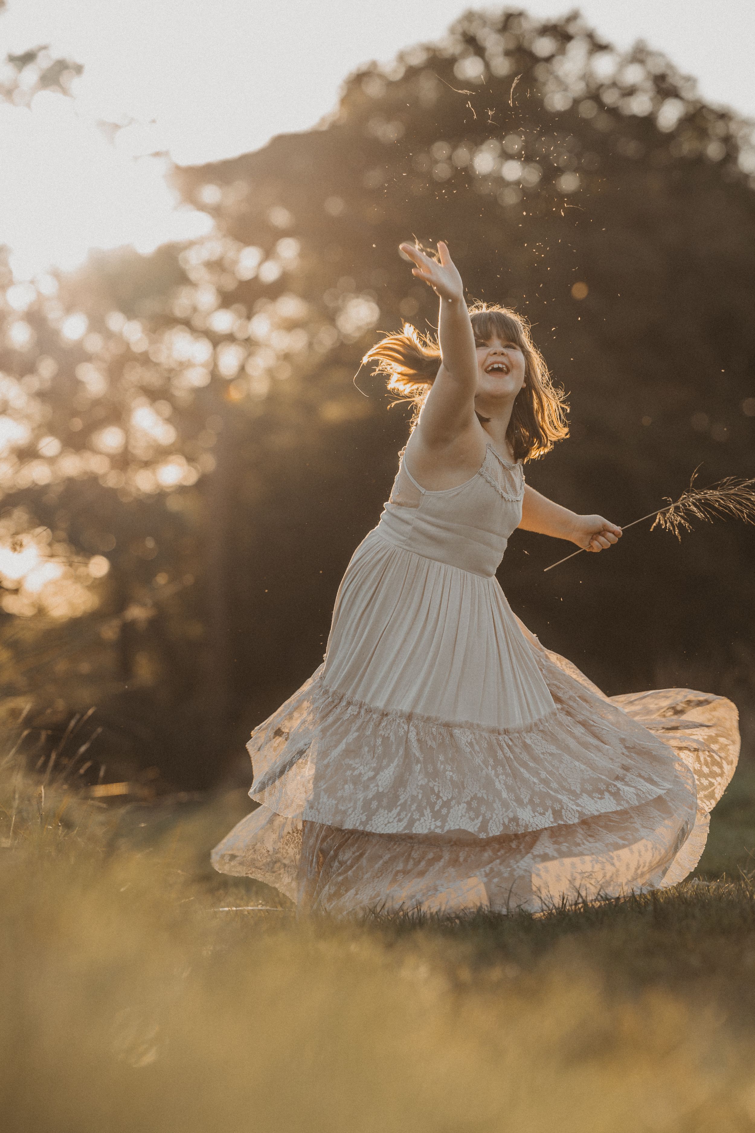 A person in a flowing white dress twirls joyfully in a sunlit meadow during golden hour.