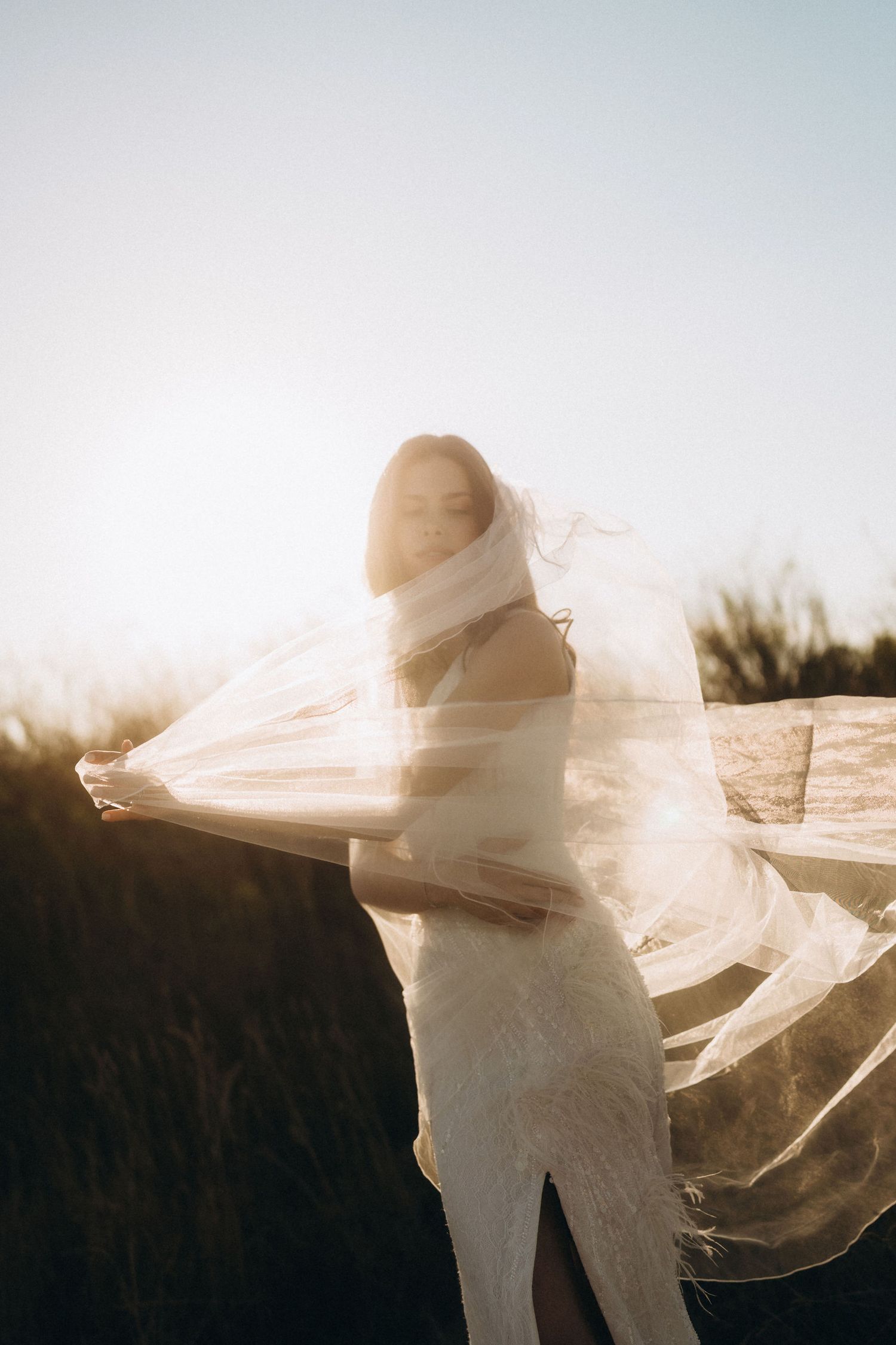 Ethereal wedding photo with bride's veil flowing in the wind during sunset.