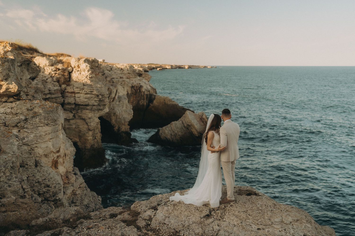 Elegant coastal wedding photography featuring a couple on rocky cliffs by the Mediterranean Sea.