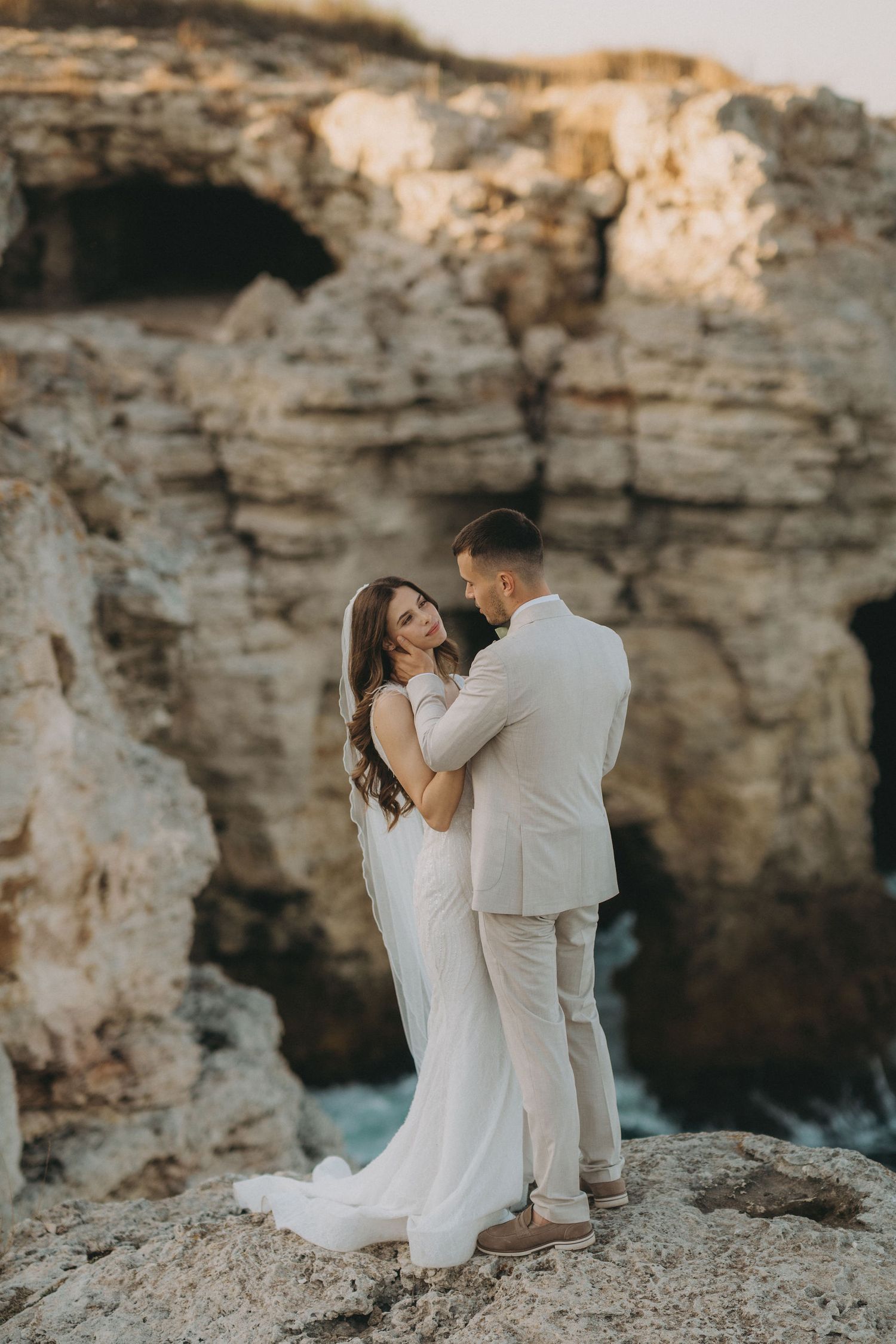 Intimate wedding moments captured on rocky coastal cliffs during sunset.