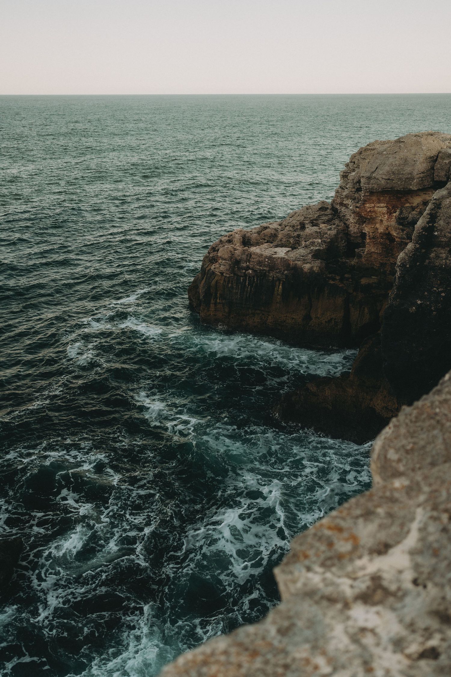 Dramatic seascape of rocky cliffs with waves crashing against limestone formations.
