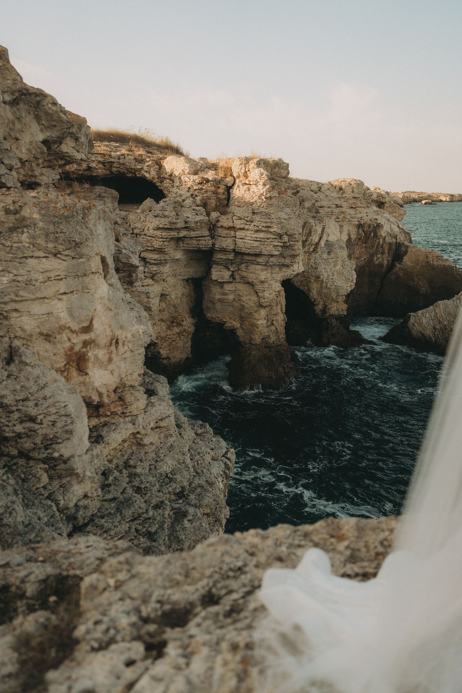 Ethereal wedding photography on Mediterranean coastal cliffs with white flowing fabric.