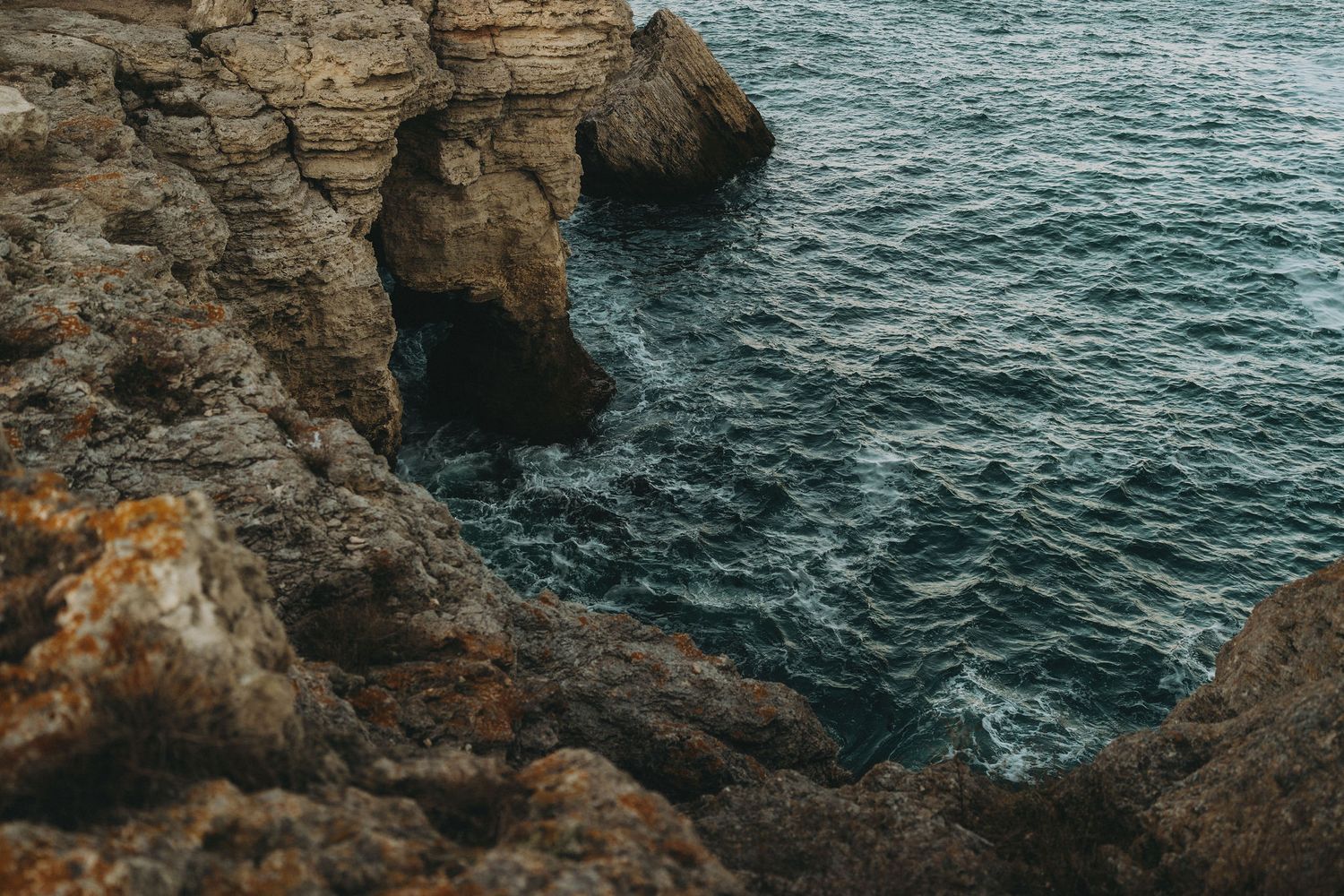 Dramatic rocky coastal cliffs meet turbulent blue ocean waters in a rugged seascape.