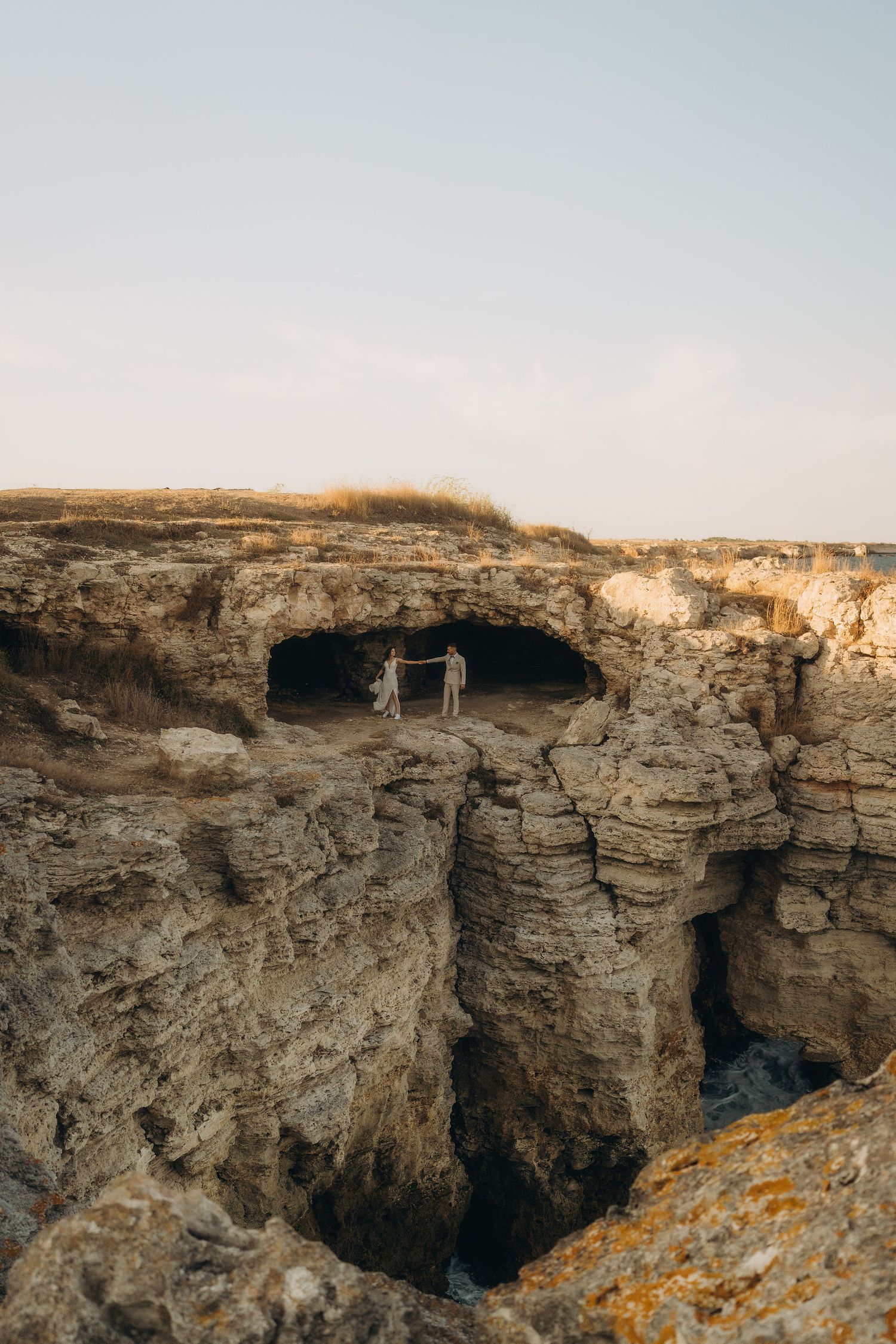 Limestone cliffs with natural cave formations stretch along a rugged coastline at sunset.