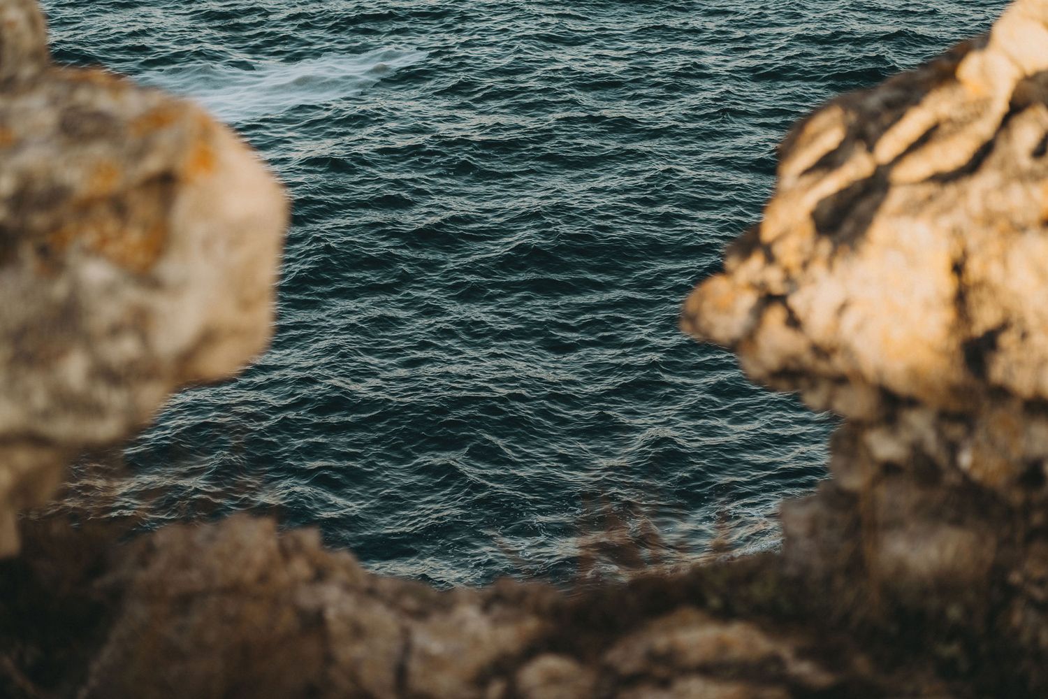 Turquoise waves crash against weathered coastal rock formations under bright sunlight.