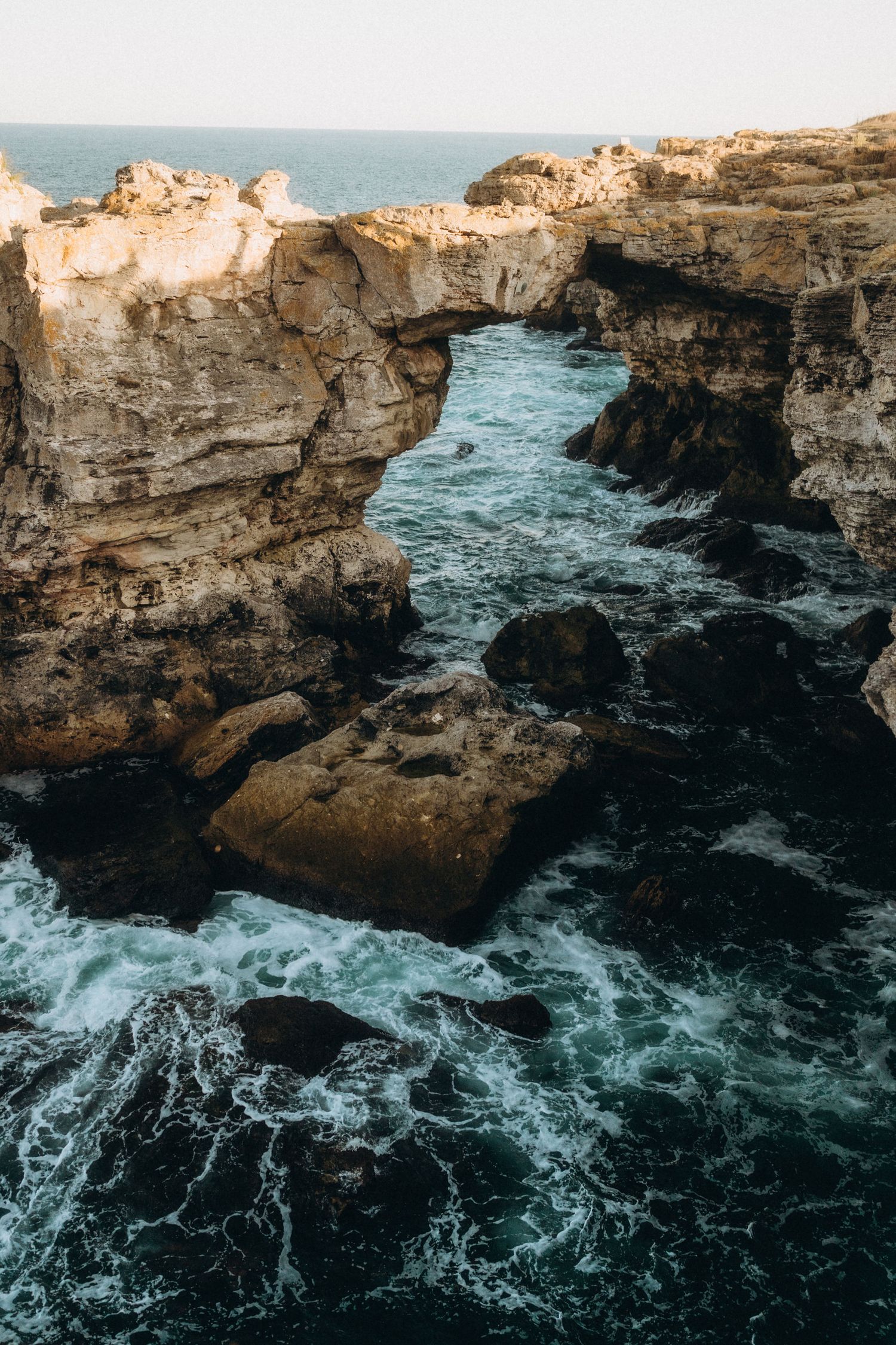 Rugged limestone cliffs tower over churning turquoise waters along a dramatic coastline.