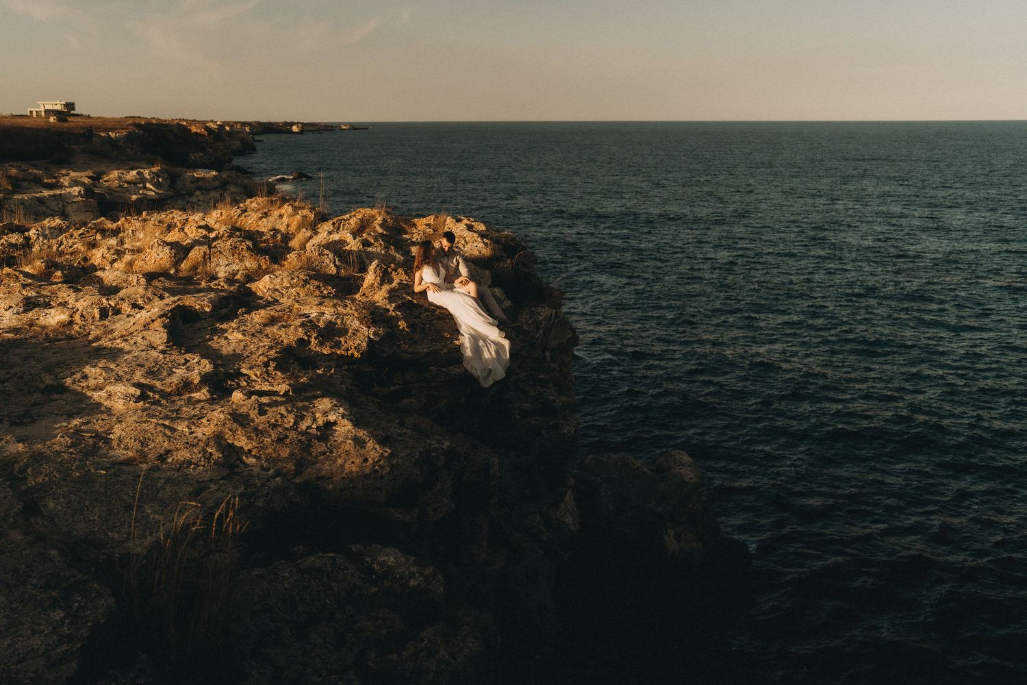 A dramatic coastal landscape with rugged cliffs and deep blue ocean waters at golden hour.