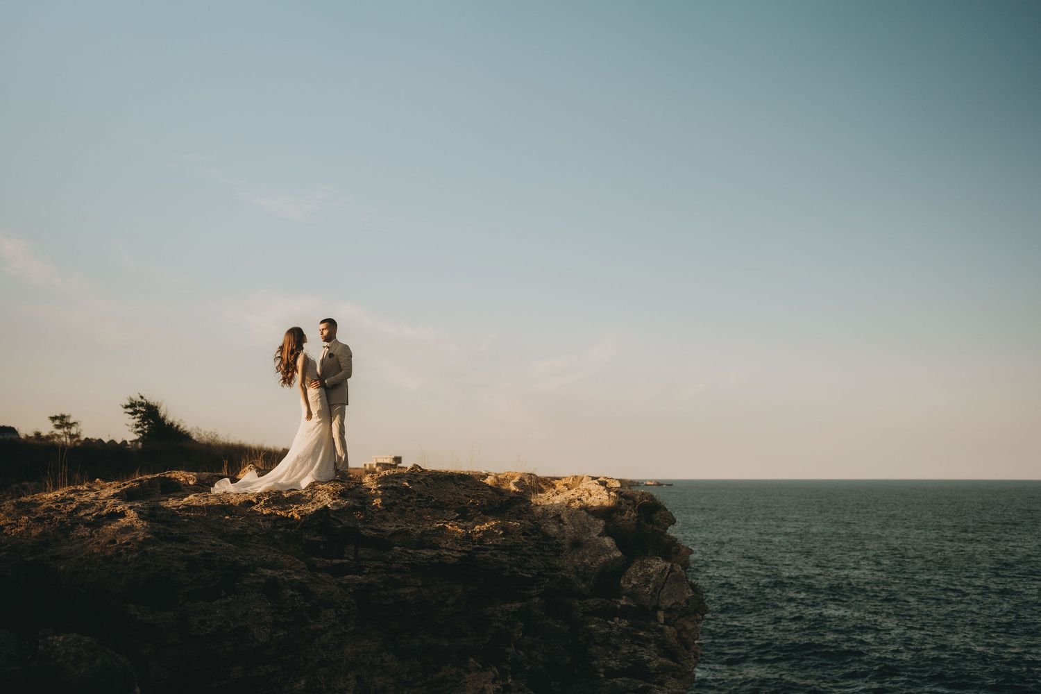 A romantic silhouette of a couple standing on a coastal cliff edge against an ocean backdrop.