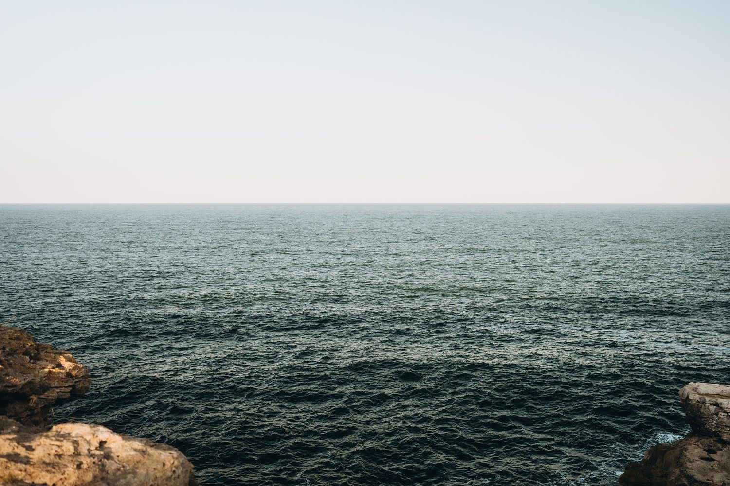 A serene seascape featuring rocky cliffs and deep blue ocean waters under a clear sky.