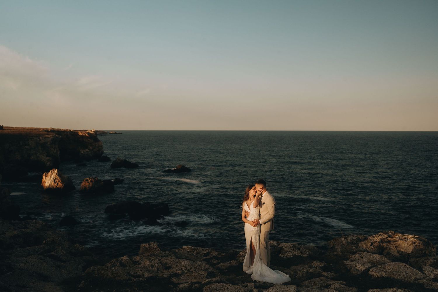 A romantic coastal portrait with dramatic cliffs and ocean waves in the background.