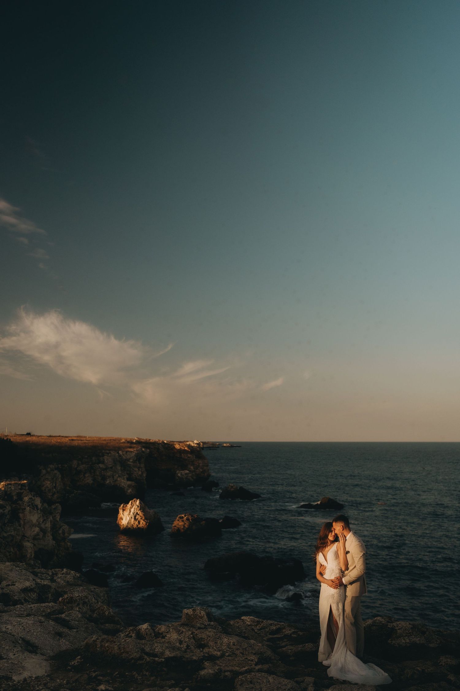 A stunning sunset wedding portrait on rugged ocean cliffs with dramatic lighting.