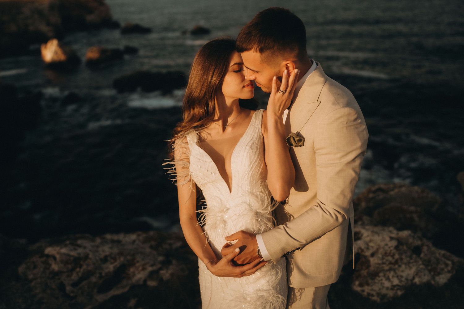 A romantic couple embraces during sunset on a rocky coastal landscape.