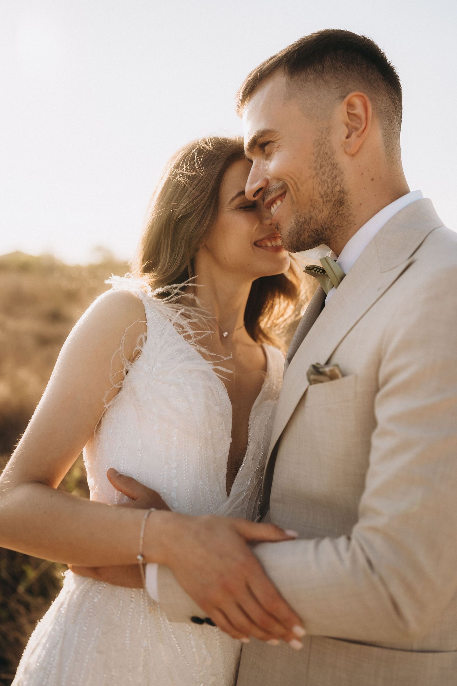 Couple in wedding attire sharing an intimate moment in warm sunlight.