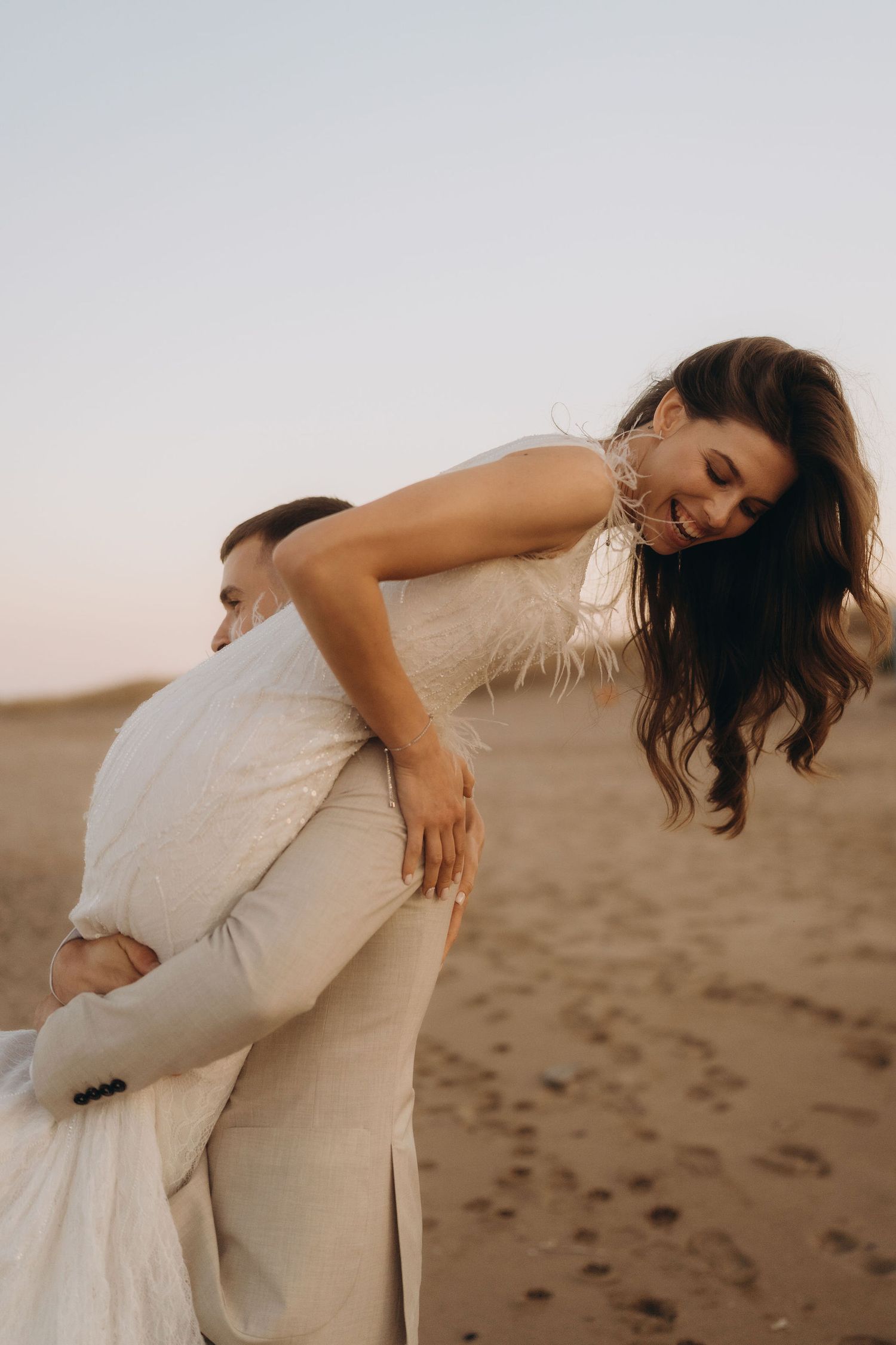 A couple in light colored outfits share intimate moments on a sandy beach.