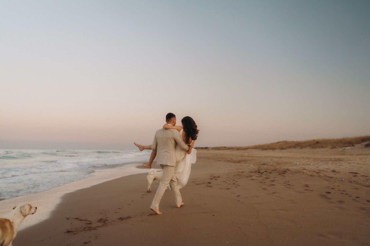 A couple dances and plays together on an empty beach at sunset.