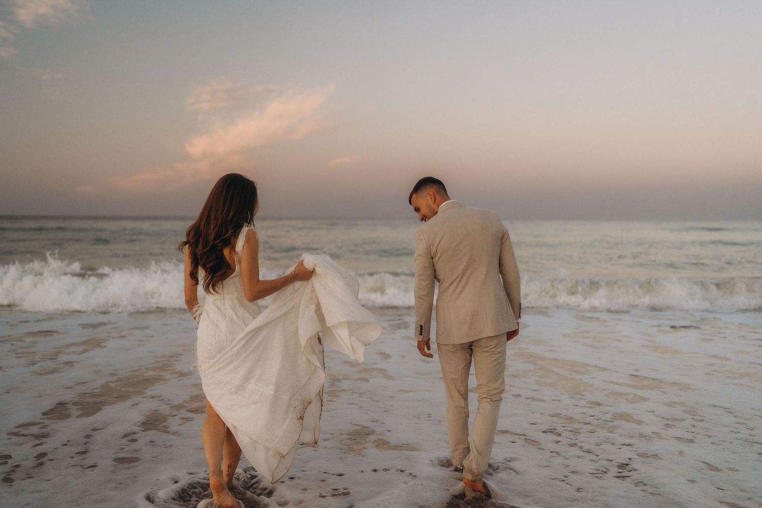 Two people dance together on a sandy beach at dusk with ocean waves rolling in.