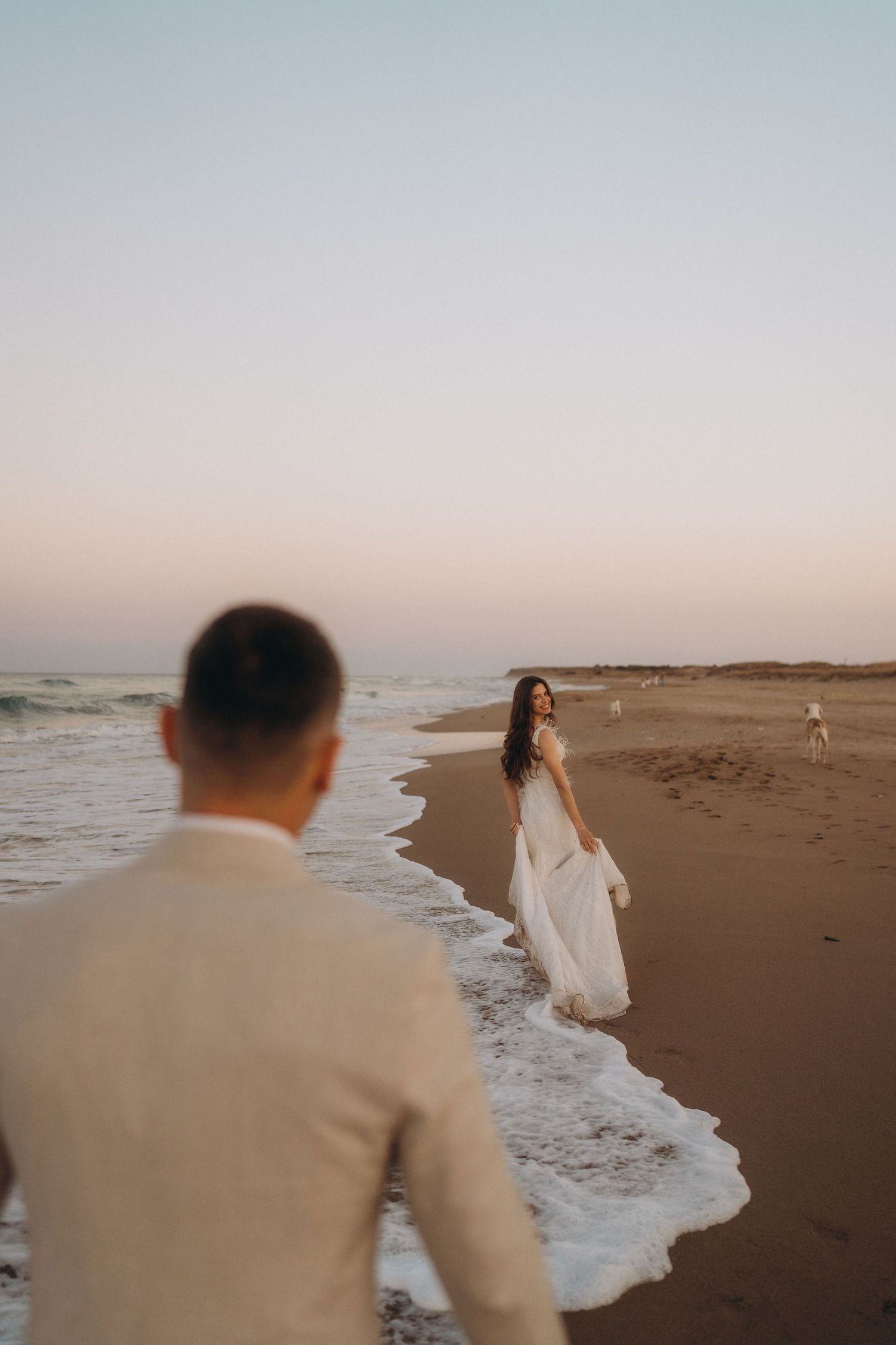 A couple shares an intimate moment on a secluded beach with waves rolling in at sunset.