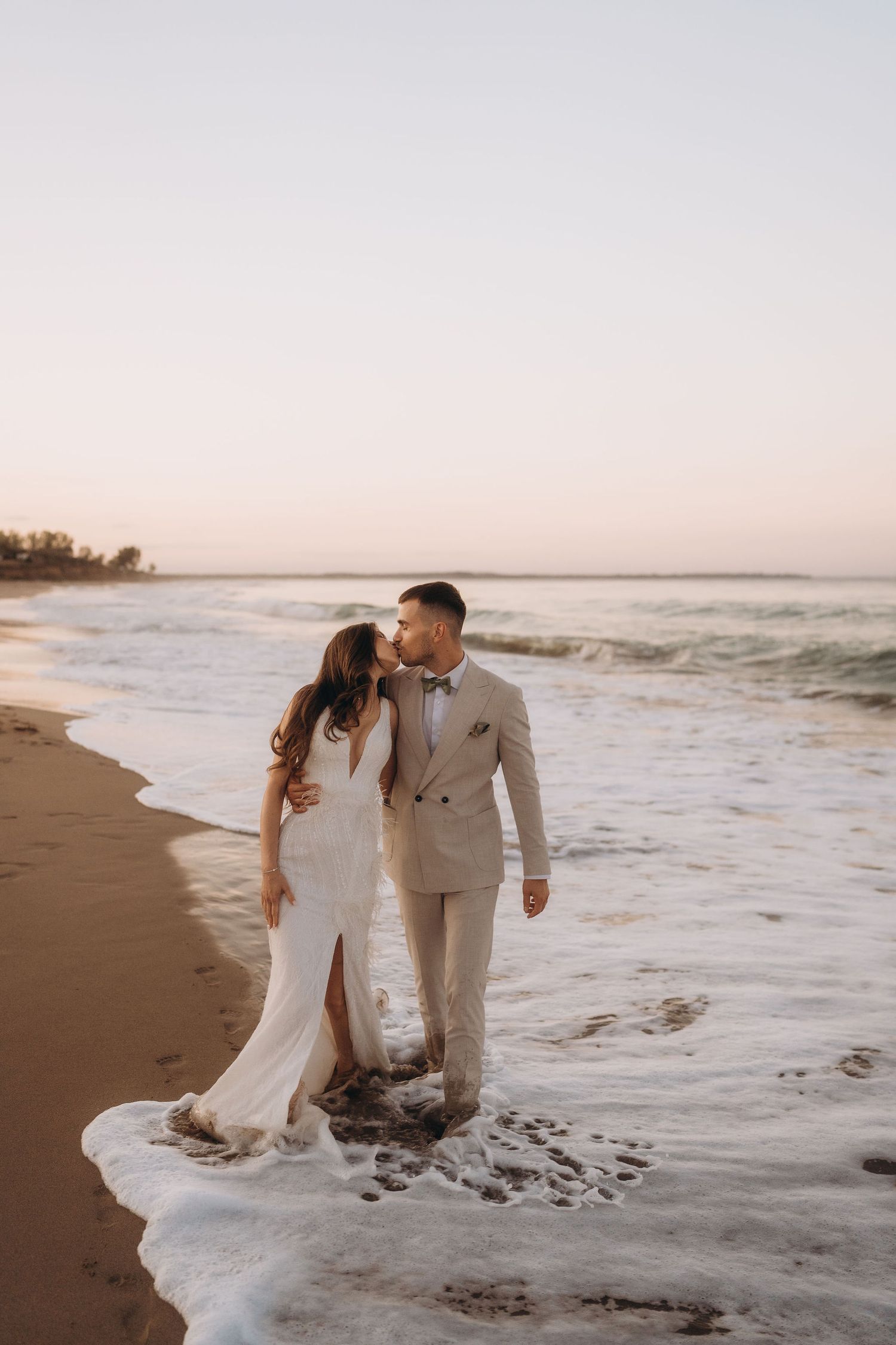 A couple sits together in the shallow waves during a romantic beach photoshoot at sunset.