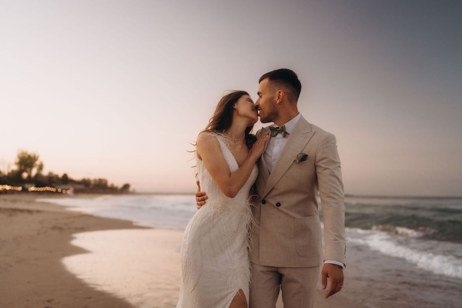 A couple in coordinated beige and white outfits share intimate moments during a beach sunset session.