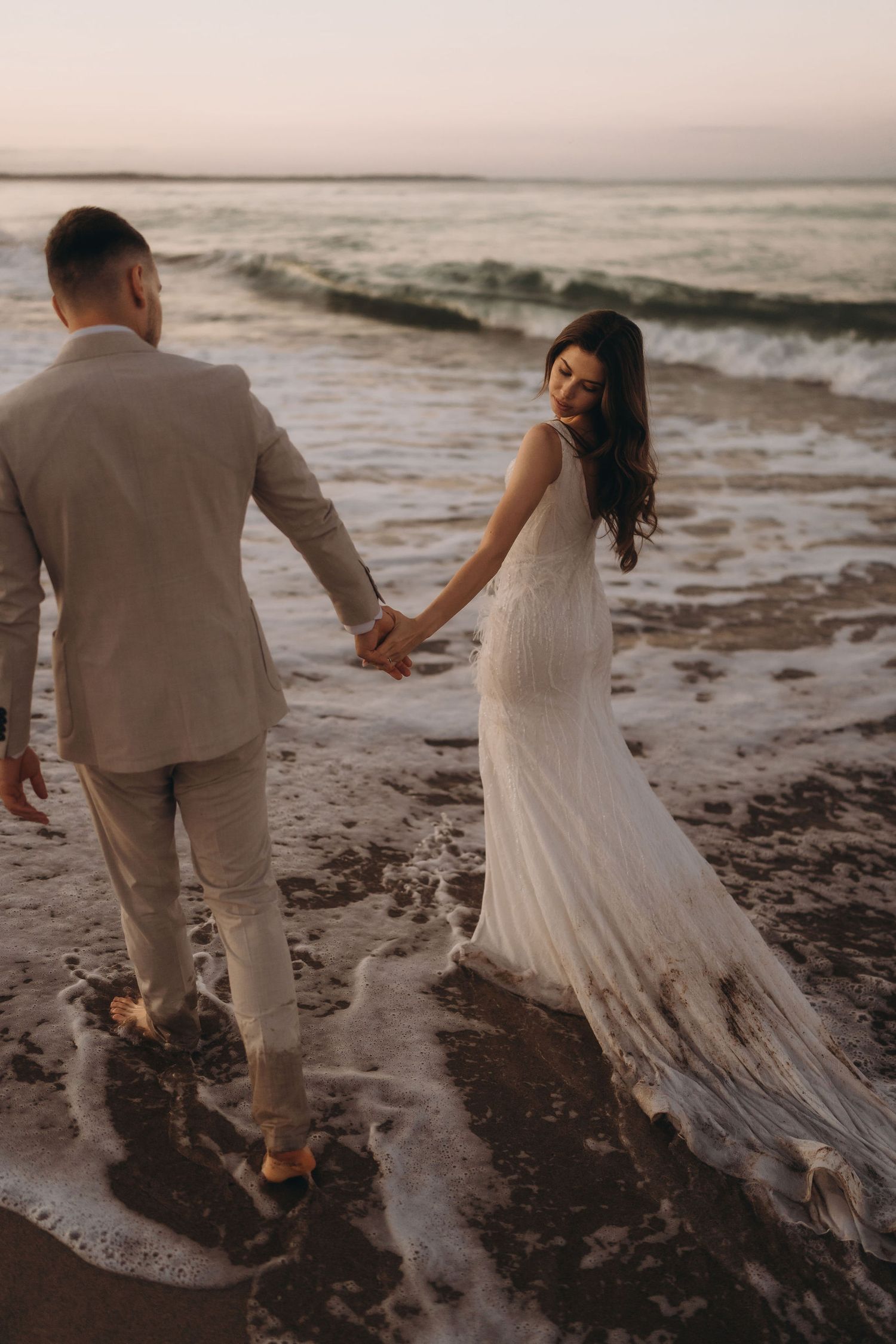 A couple splashes through ocean waves at the beach during golden hour.