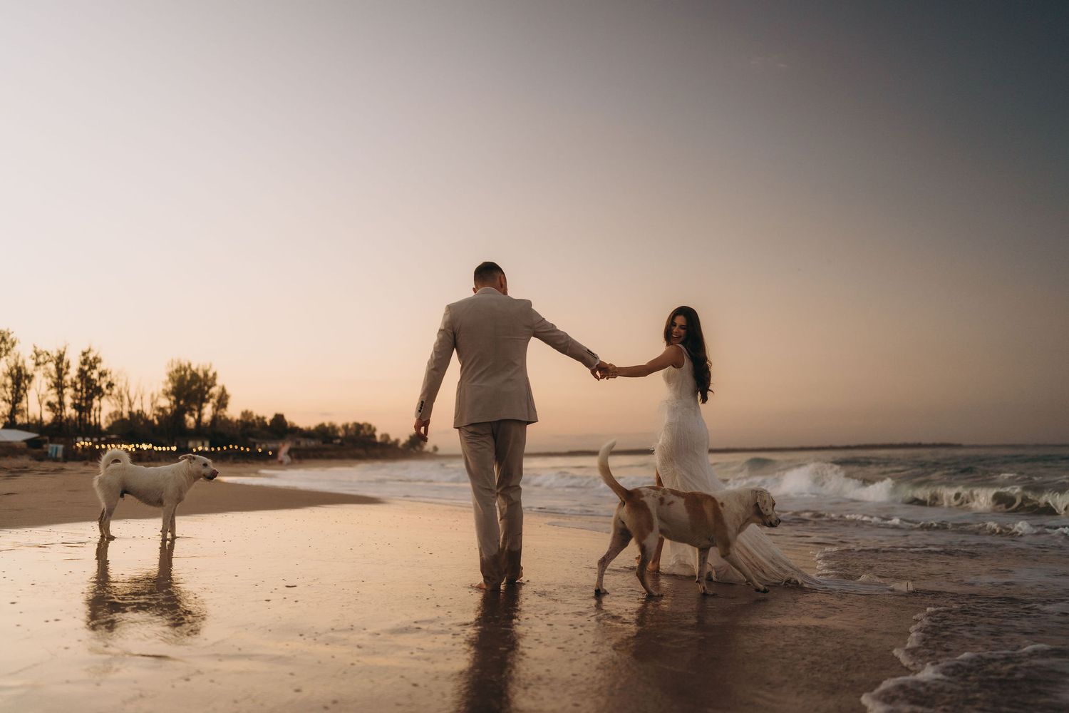Silhouettes of a couple walking along a beach at sunset with waves crashing nearby.