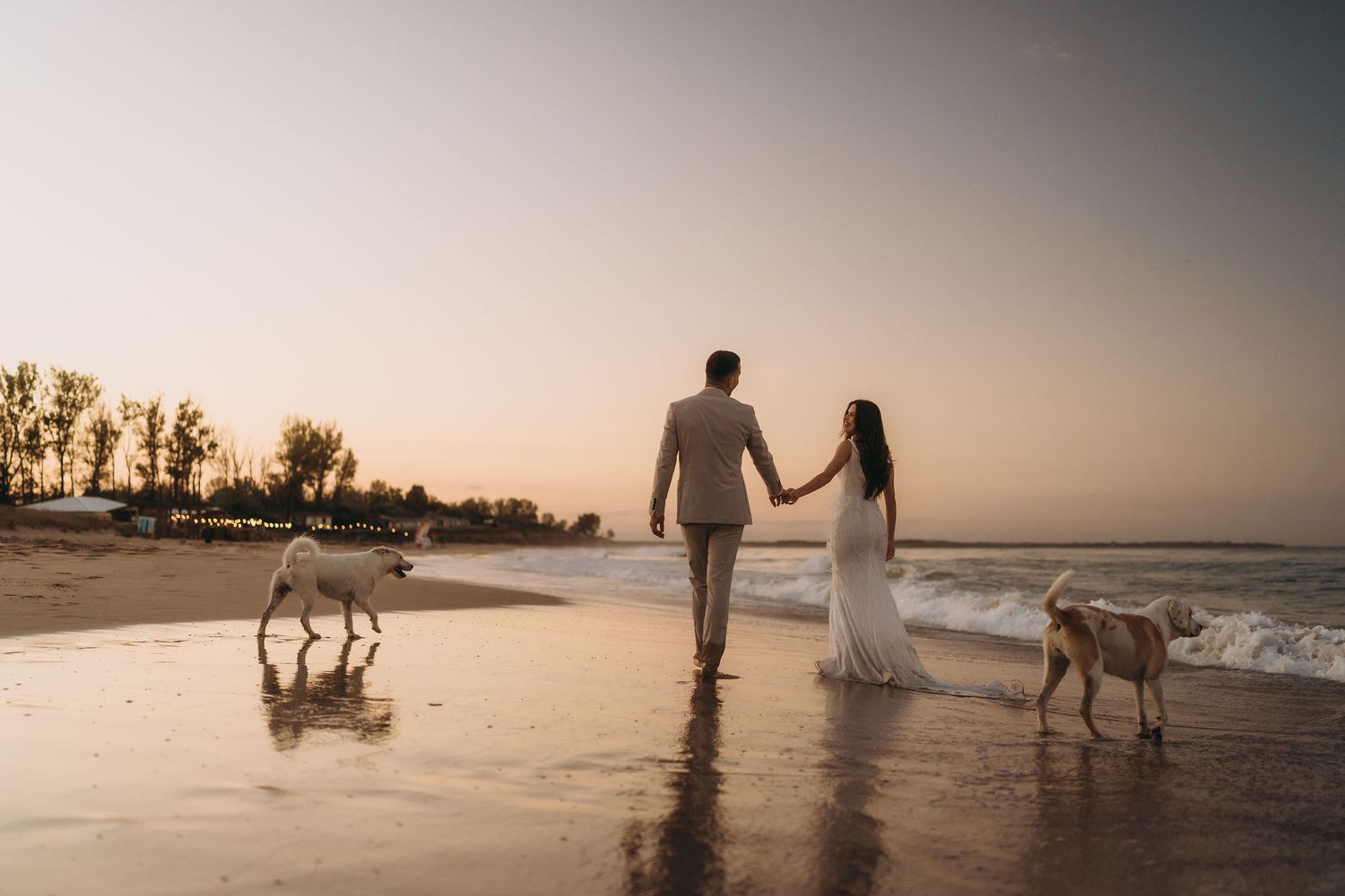 Silhouetted figures stroll along a peaceful beach during a golden sunset.