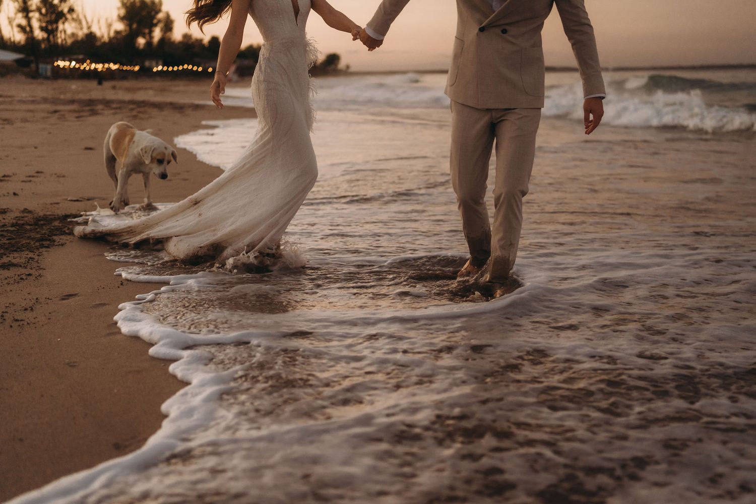 Legs and feet of a couple walking through gentle ocean waves at sunset.