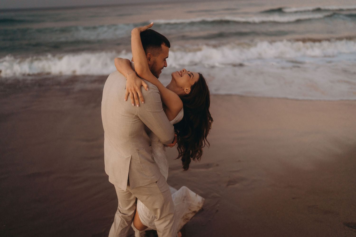A romantic beach photoshoot featuring a couple in light-colored attire by the ocean.