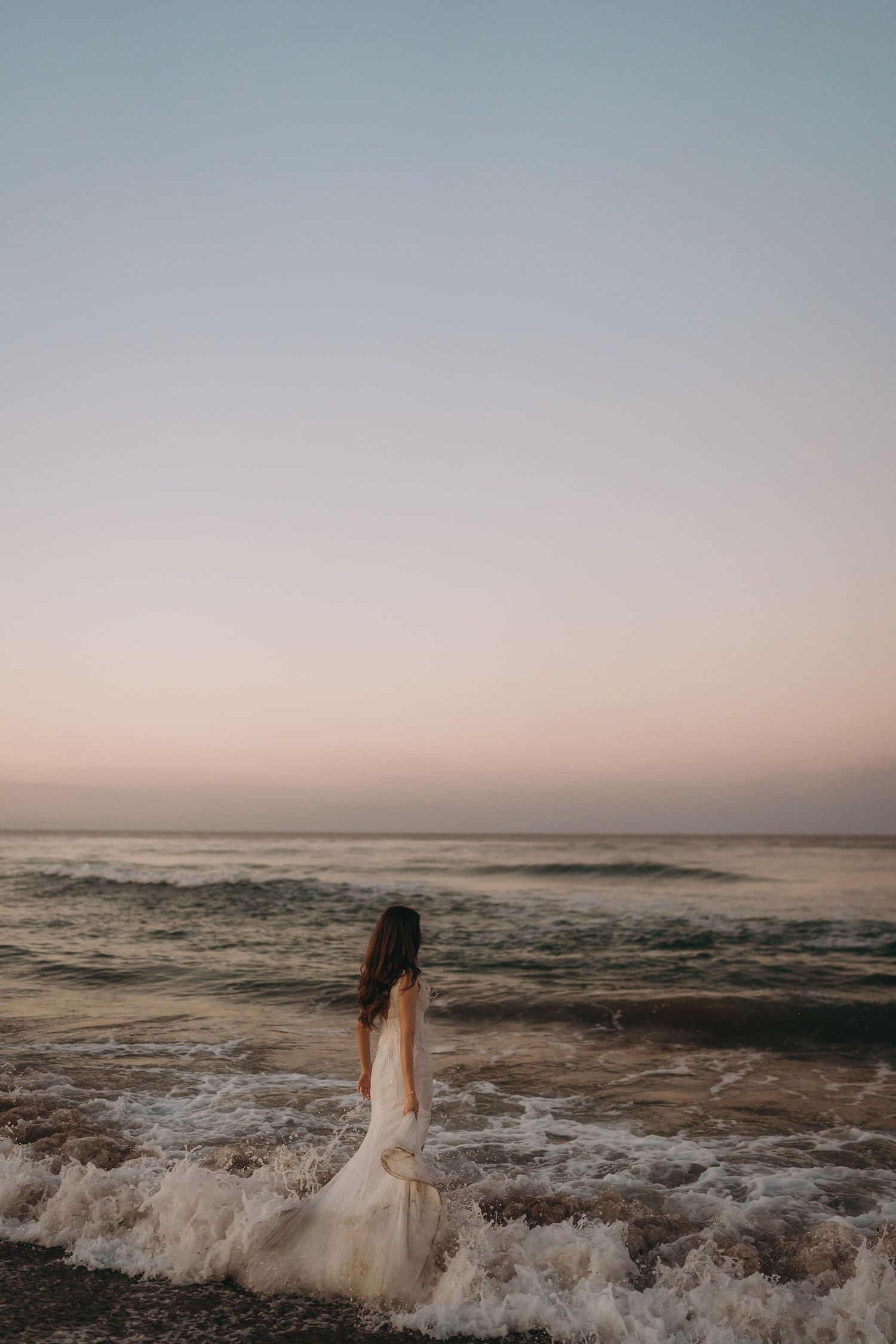 Ocean waves crash dramatically on a beach during a misty sunset.