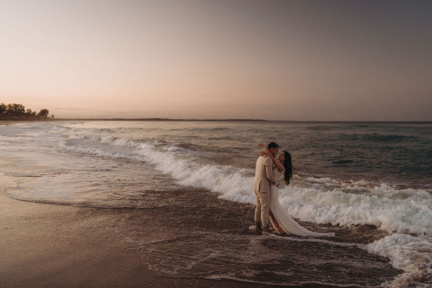 A couple enjoys a tender moment by the crashing waves at sunset.