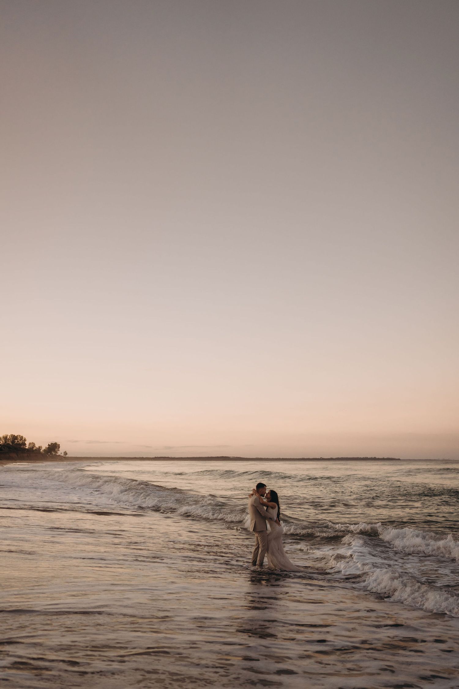 Silhouettes wade through gentle ocean waves during golden hour at the beach.