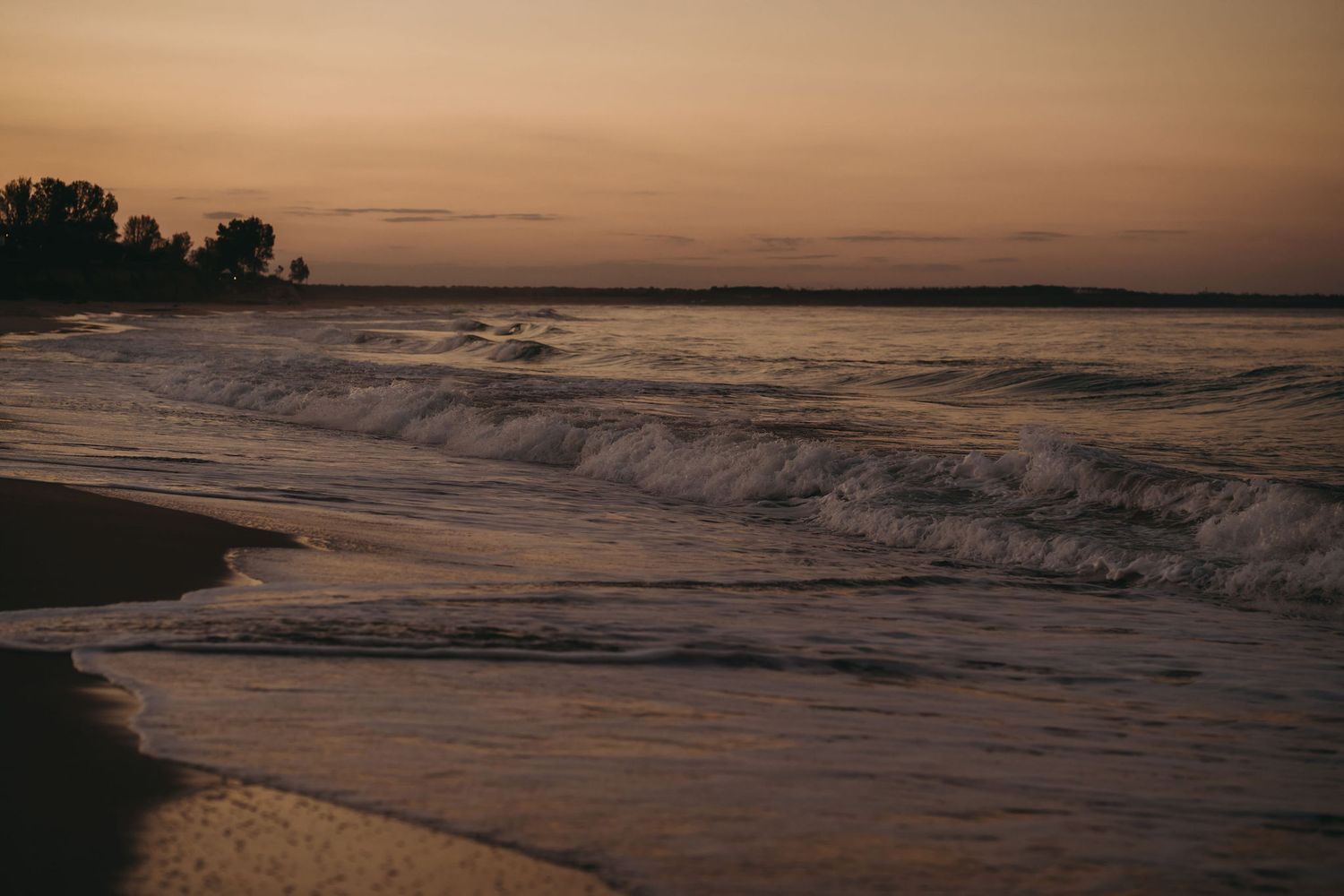 Sunset casts golden light across beach waves and shoreline.