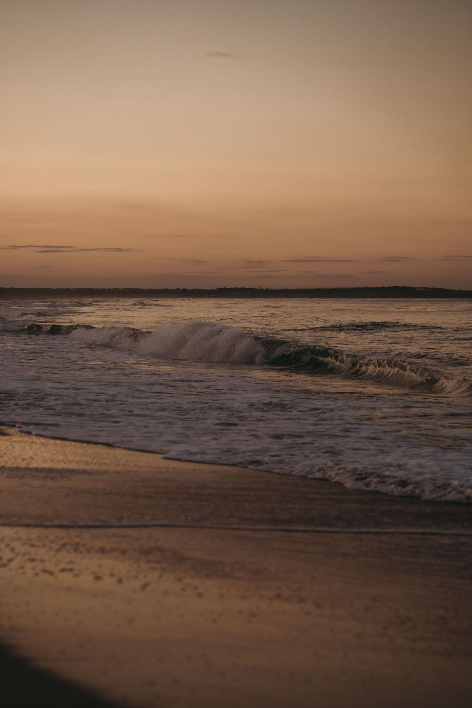 Waves roll onto sandy beach during golden hour with warm tones in the sky.