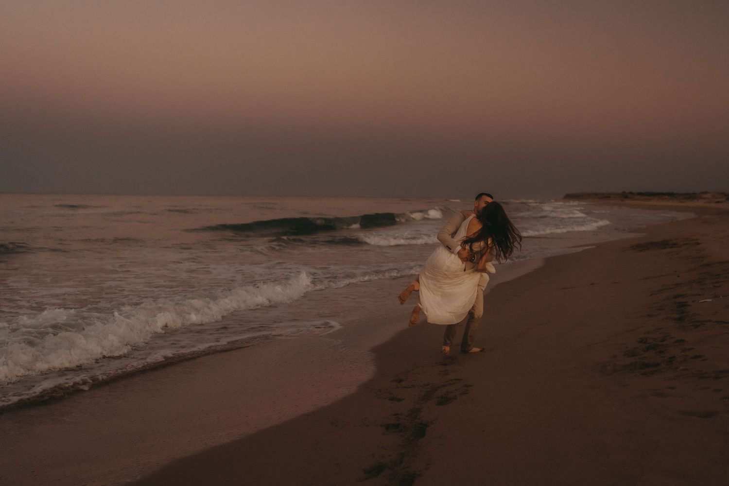 People enjoying playful moments on beach at sunset.