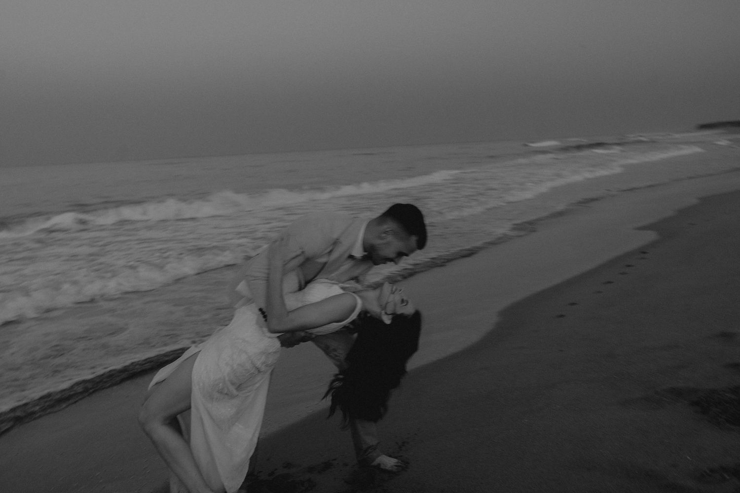 Figures play and dance along the shoreline at dusk.