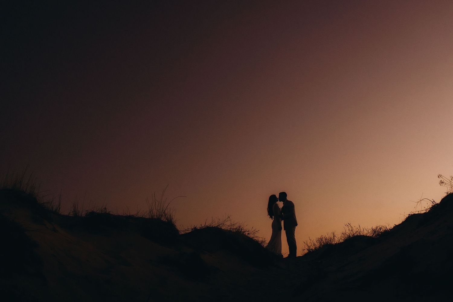 Dark figures stand on coastal cliff edge at twilight.